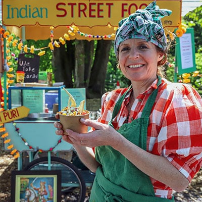 Woman in front of Indian street food cart holding up a portion of food