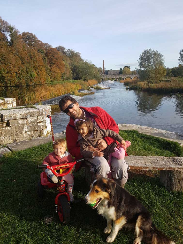 Man sitting on bench in front of river with kids and a dog